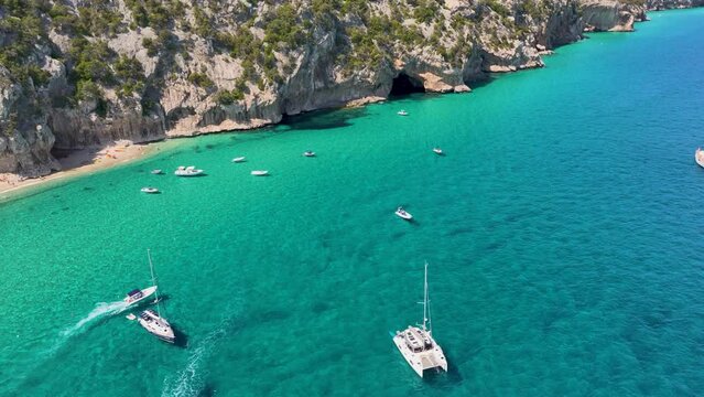 Aerial shot - A few boats near Sardinian coastline with turquoise blue water underneath.