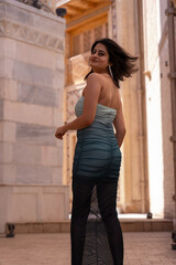 A woman in a blue and black dress stands in front of a building