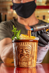Barman sets fire to cinnamon in tiki cocktail at the bar. Summer party background.