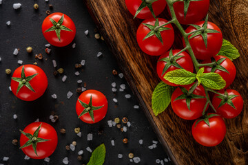 Fresh cherry tomatoes on a black background with spices. Food background. Top view.