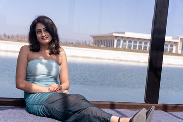 A woman is sitting on a ledge by a body of water, wearing a blue dress