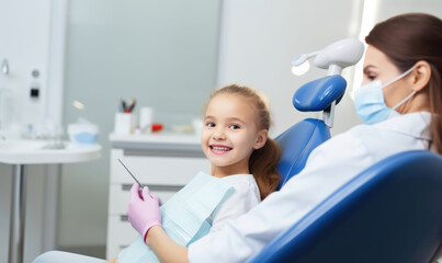 Little cute girl sitting in dental chair while doctor fixing her teeth. Dental care concept.