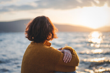 Young mature woman looking at the sunset on the seashore in the rays of the sun