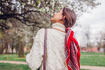 Back view of stylish woman walking with red hair scarf in spring park. Retro female fashion. Headscarf for bun hairstyle