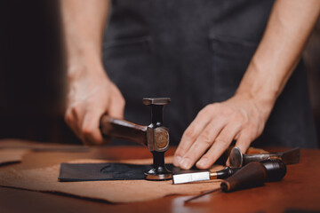Tailor processing hammers seam on leather goods, handmade craftsman. DIY craft product from skin