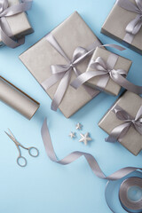 Gift wrapping. Gray paper, silver ribbon, scissors on light blue background. Vertical, place for text