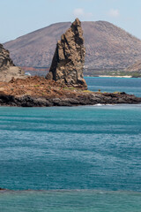 pinaculo de roca volcánica con volcán de fondo en bahía de agua turquesa en Galápagos