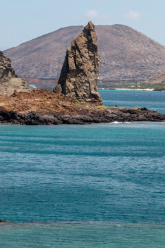 pinaculo de roca volc&aacute;nica con volc&aacute;n de fondo en bah&iacute;a de agua turquesa en Gal&aacute;pagos
