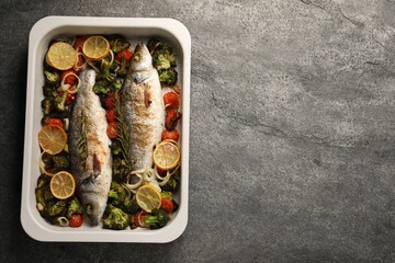 Delicious fish with vegetables and lemon in baking dish on grey textured table, top view. Space for...