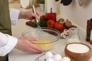 Woman whisking eggs in bowl at light table indoors, closeup