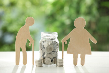 Pension savings. Figures of senior people and jar with coins on white table against blurred green...