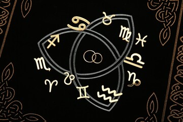 Zodiac signs and wedding rings on book, flat lay