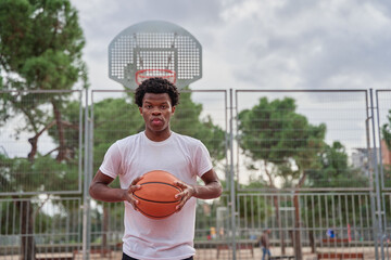 Young handsome african american man basketball player holding ball with both hands and smiling...