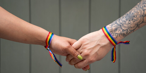 Hands of unrecognizable lesbian female couple with LGBT rainbow bracelet
