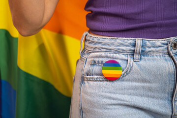 Close-up of an unrecognisable lesbian woman with a rainbow pin and flag. Support of LGBTQ community and pride concept.