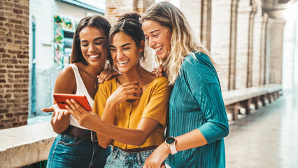 Three happy friends watching a smart phone mobile outdoors - Millennials women using cellphone on city street - Technology, social, friendship and youth concept - obrazy, fototapety, plakaty
