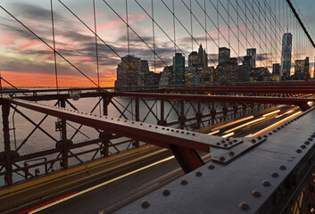New York skyline from Brooklyn Bridge at sunset showing car lights trails in foreground