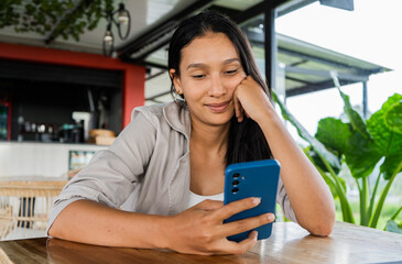 joven adolescente sentada en un café leyendo mensajes en su celular  - obrazy, fototapety, plakaty