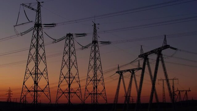Silhouette of high-voltage poles against the background of the sunset sky. Power tower. Distribution of high voltage current along the power line. Electrical substation