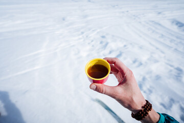 Small cup of coffee in nature, hand holding glass of tea on snow background, warming drink in winter.