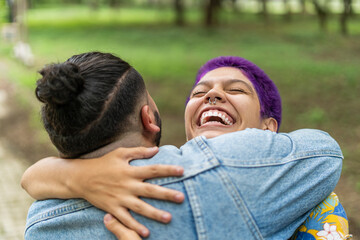 Close up image of two very smiling gay friends greeting each other with a big hug outdoors. 