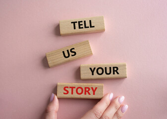 Tell us your story symbol. Concept words Tell us your story on wooden blocks. Beautiful pink background. Businessman hand. Business and Tell us your story concept. Copy space.