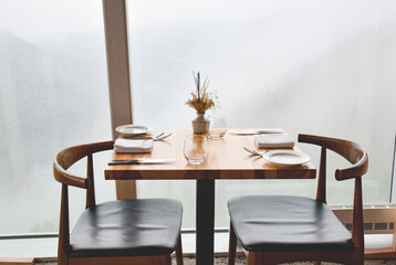 Minimalistic natural colored wood table set at a restaurant ready for customers in front of large window
