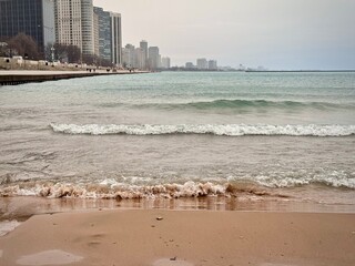 view of a sandy beach on Lake Michigan in Chicago with the city buildings in the background on a...