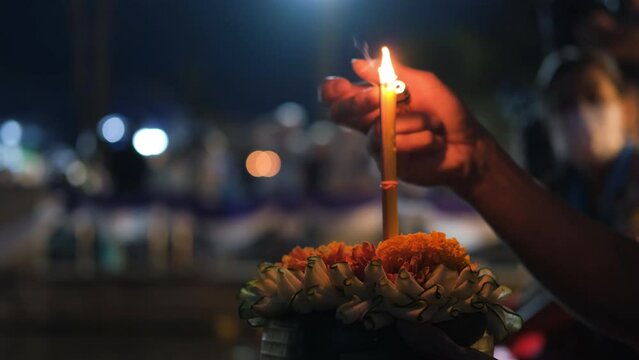 Close-up of hand of unrecognizible man lighting candle in Loy Krathong while praying to water goddess, selective focus