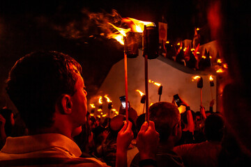 Um fiel de costas e várias outras pessoas vestidas de túnica e segurando uma tocha de fogo em procissão religiosa em Goiás. Procissão do Fogaréu. 