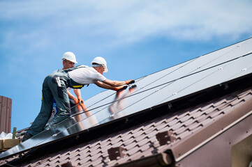 Workers building photovoltaic solar panel system on rooftop of house. Men technicians installing...