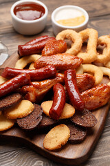 Set of assorted beer snacks - grilled sausages, roasted chicken wings, croutons, deep fried onion rings and squid rings on wooden board with sauce. Close up view