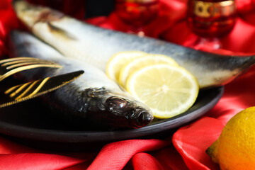 Fish menu: herring on a black plate, cutlery, lemon slices nearby, close-up