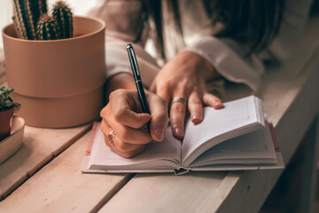 Close-up of female hands writing in a notebook.A woman is lying on a windowsill with indoor plants.
