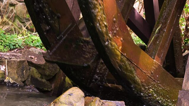 Age-worn wooden spokes of waterwheel interplay with gentle cascade of the stream. This tranquil scene is framed by natural texture of stones. Water cycle and conservation. Historical machinery working