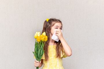 A girl holds a bouquet of spring flowers and covers her nose against allergy symptoms.
