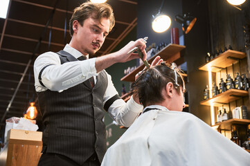Professional hairdresser in fancy outfit cutting hair. Man with a French mustache styling client's...