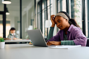 Black female student feeling bored while e-learning on laptop at university.