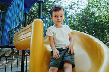 happy child kindergarten boy playing on a slide on the playground in summer