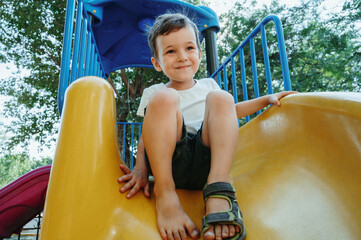 happy child kindergarten boy playing on a slide on the playground in summer