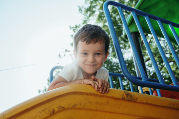 happy preschooler boy playing on a slide on the playground in summer