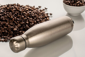 One metal thermos bottle on the table with fragrant roasted coffee beans, macro. - obrazy, fototapety, plakaty