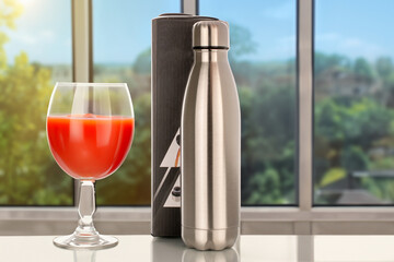 One metal thermos bottle with a paper box and a glass of tomato juice stands on the table, close-up, against the background of the window. - obrazy, fototapety, plakaty