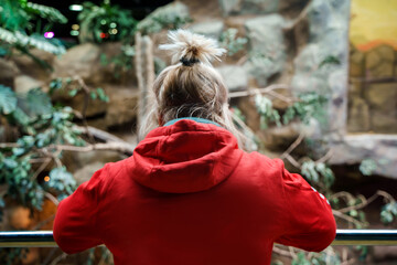A woman in a red hoodie stands on the second floor and looks at the landscaping from below at the zoo