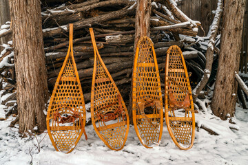 Classic wooden snowshoes, Huron and Bear Paw, against a pile of firewood