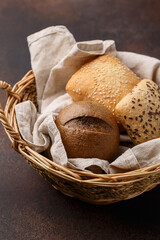 Different kinds of freshly baked buns. White, multigrain and rye buns in wicker basket on dark concrete background