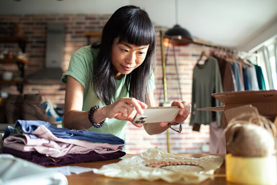Smiling Asian woman packing clothes into a box at home