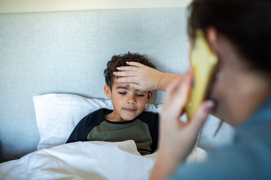 Mother checking sick child's temperature in bed while on the phone