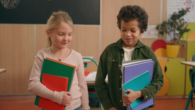 Two happy naughty pupils children diverse multiethnic kids African American boy and Caucasian girl classmates friends having fun funny pushing each other showing tongues fooling tease at school class