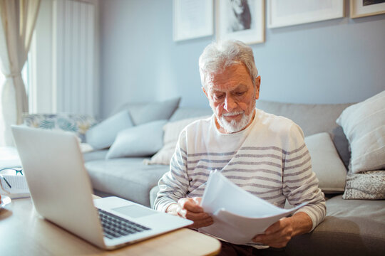 Stressed senior man with laptop and paperwork at home